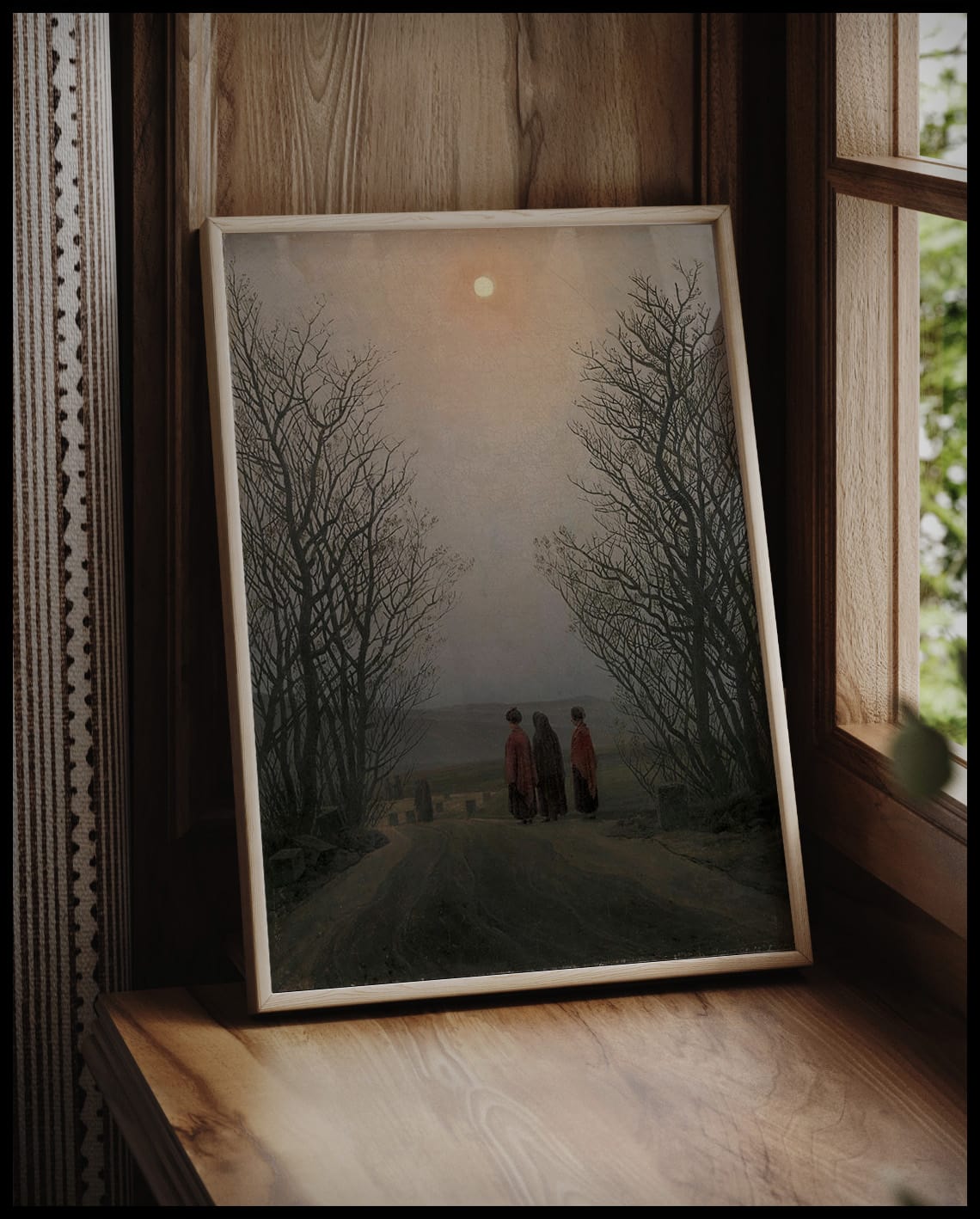 Ein gerahmter Kunstdruck mit drei Personen auf einem Weg, eingerahmt von kahlen Bäumen, vor einem Fenster an die Wand angelehnt
