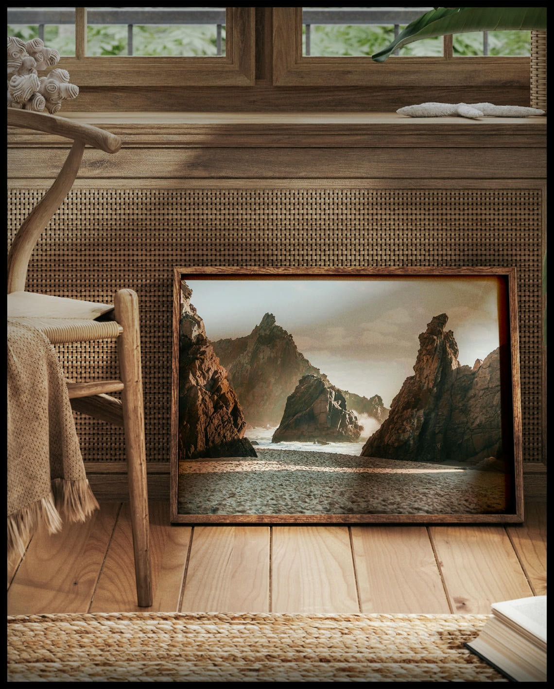 Ein gerahmtes Poster von hohen Felsformationen im Meer an einem Sandstrand, vor einem Fenster an die Wand angelehnt