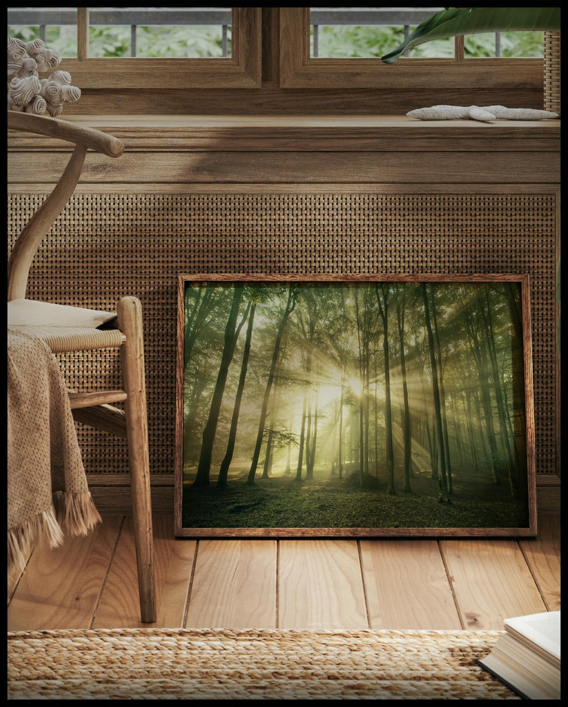 Ein gerahmtes Poster von Sonnenstrahlen die in einem Wald durch schmale Bäume hindurch scheinen, vor einem Fenster an die Wand angelehnt