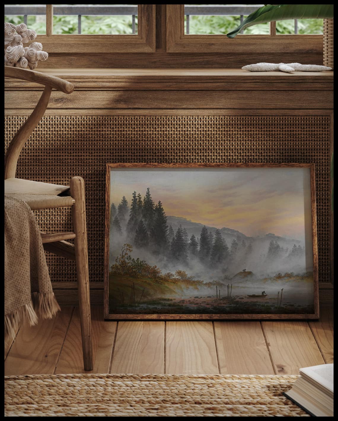 Ein gerahmter Kunstdruck von einer Morgenszene mit einer Waldlandschaft, angedeutetem Sonnenaufgang und einem Fischerboot, vor einem Fenster an die Wand angelehnt