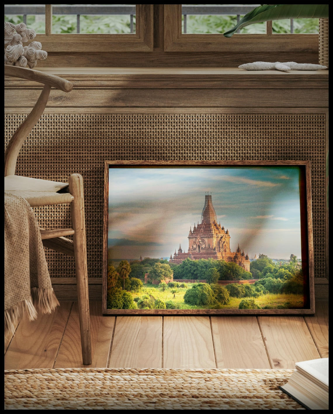 Ein gerahmtes Poster von einem hohen Tempel inmitten einer bewachsenen Landschaft, vor einem Fenster an die Wand angelehnt