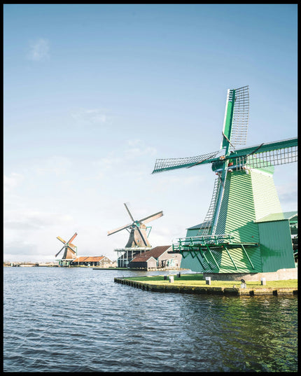 Ein Poster von drei Windmühlen aus Holz die am Wasser stehen. 