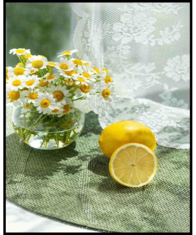 Ein Poster von zwei Zitronen und Blumen in einem Glas auf einer grünen Unterlage aus Stoff.