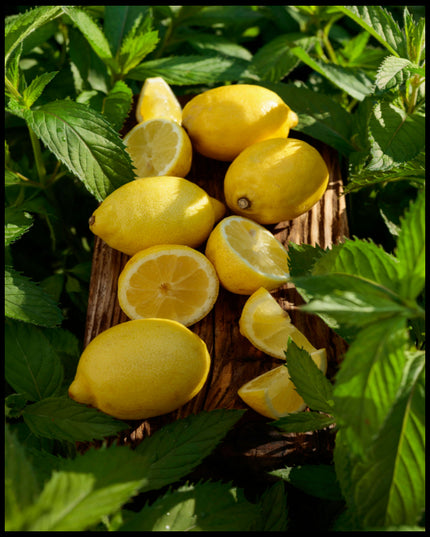 Ein Poster von mehreren Zitronen und Zitronenstücken auf einem Holzbrett umgeben von grünen Blättern.