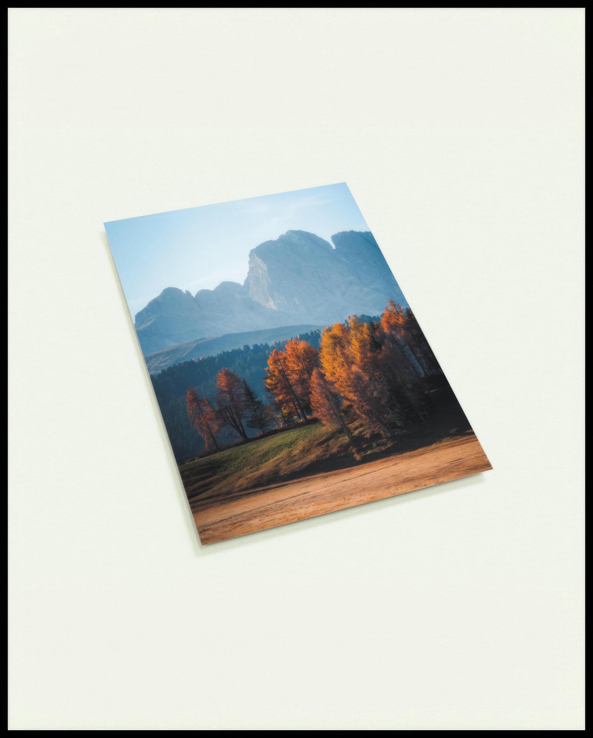Eine Postkarte von herbstlich gefärbten Bäumen vor einer Berglandschaft in den Dolomiten.
