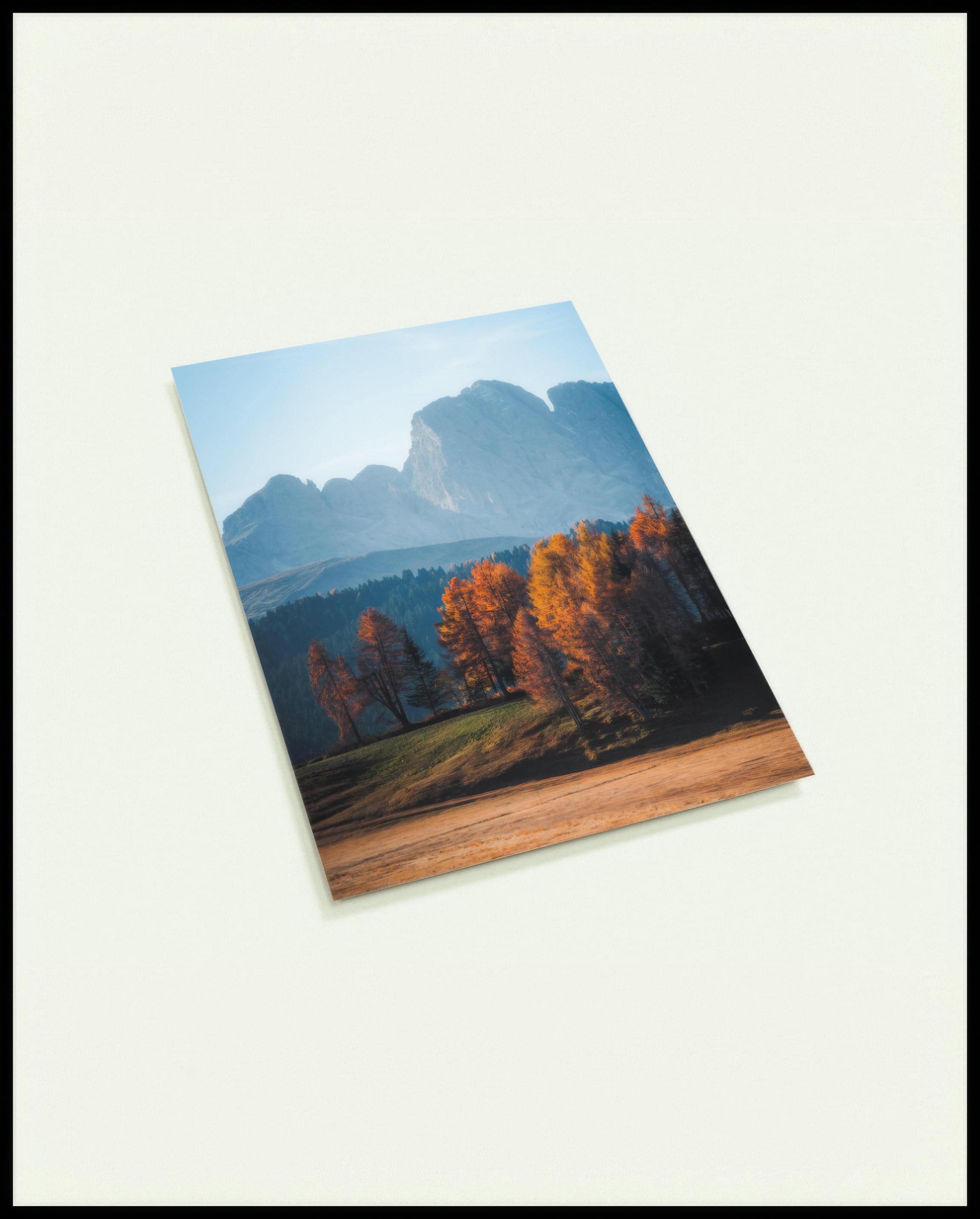 Eine Postkarte von herbstlich gefärbten Bäumen vor einer Berglandschaft in den Dolomiten.