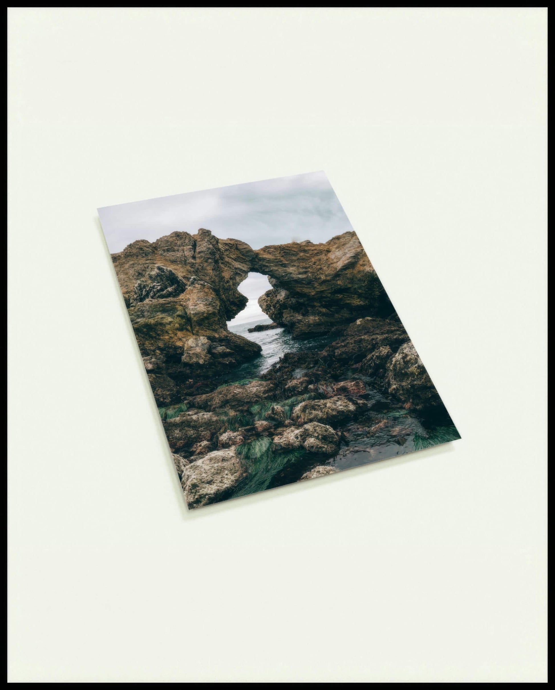 Eine Postkarte von einer felsigen Küste mit einer natürlichen Felsformation, die ein Fenster zum Meer bildet.