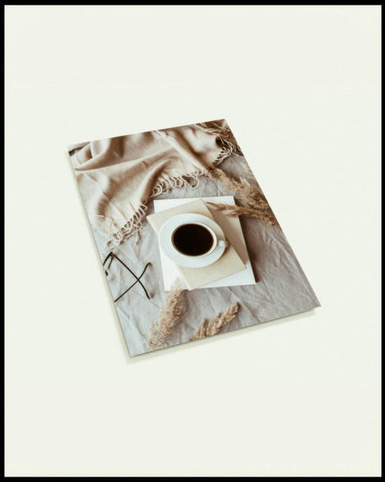 Eine Postkarte von einer Tasse Kaffee auf einem Stapel Bücher, umgeben von einem beigen Tuch und getrockneten Pflanzen.