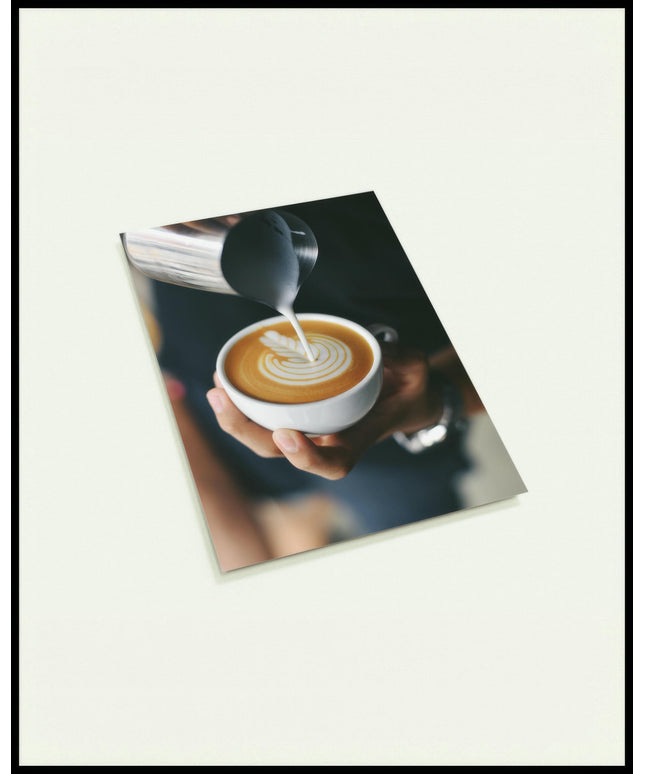 Eine Postkarte von einem Barista, der kunstvoll Milch in eine Tasse Kaffee gießt und ein Muster kreiert.