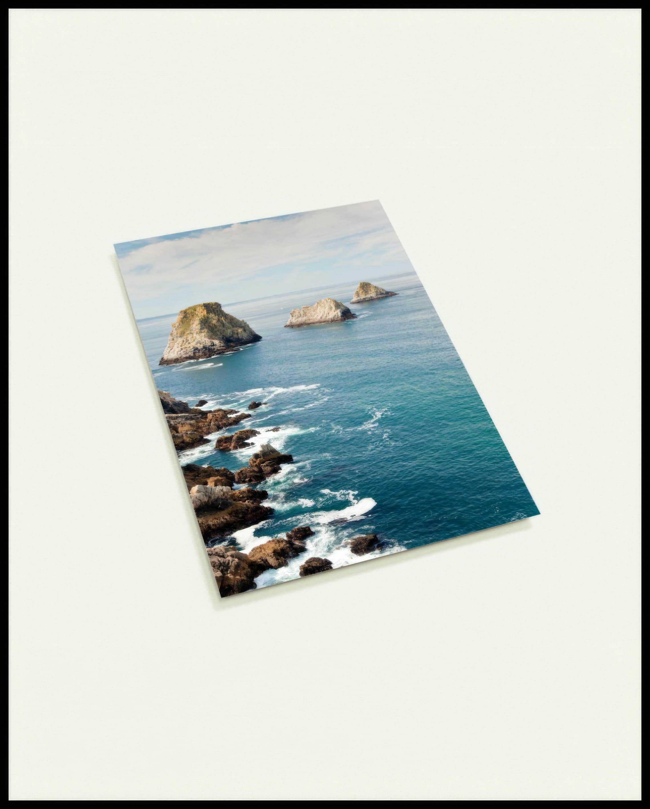 Eine Postkarte vom Blick auf das blaue Meer und mehrere Felsformationen die aus dem Wasser blicken.