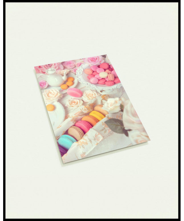 Eine Postkarte von bunten Macarons, arrangiert auf einem Tisch mit rosa Rosen und weißem Porzellan.