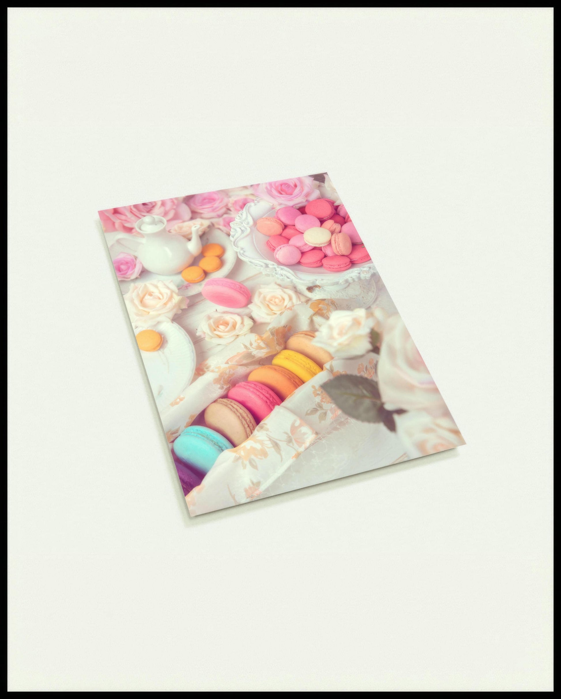 Eine Postkarte von bunten Macarons, arrangiert auf einem Tisch mit rosa Rosen und weißem Porzellan.