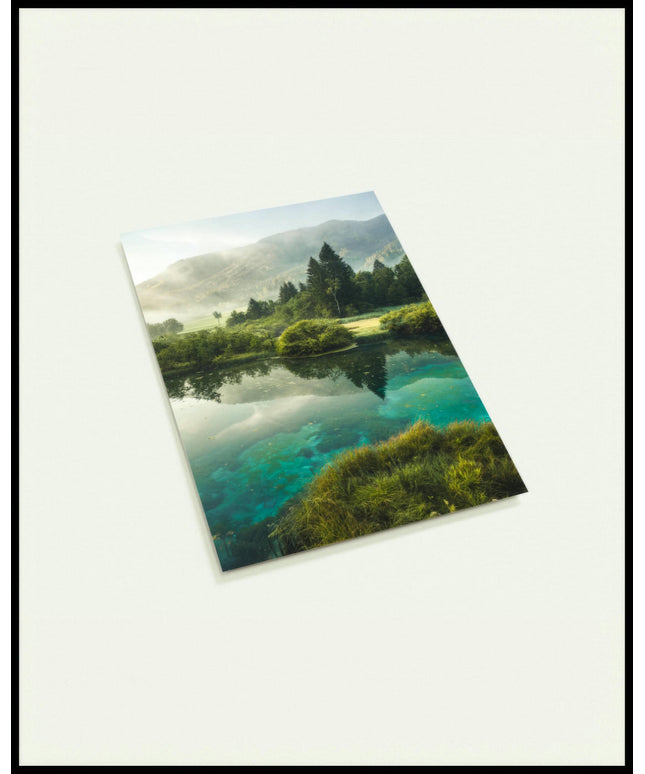 Eine Postkarte von einem See der von Büschen, Bäumen, Strand und Bergen umgeben ist.