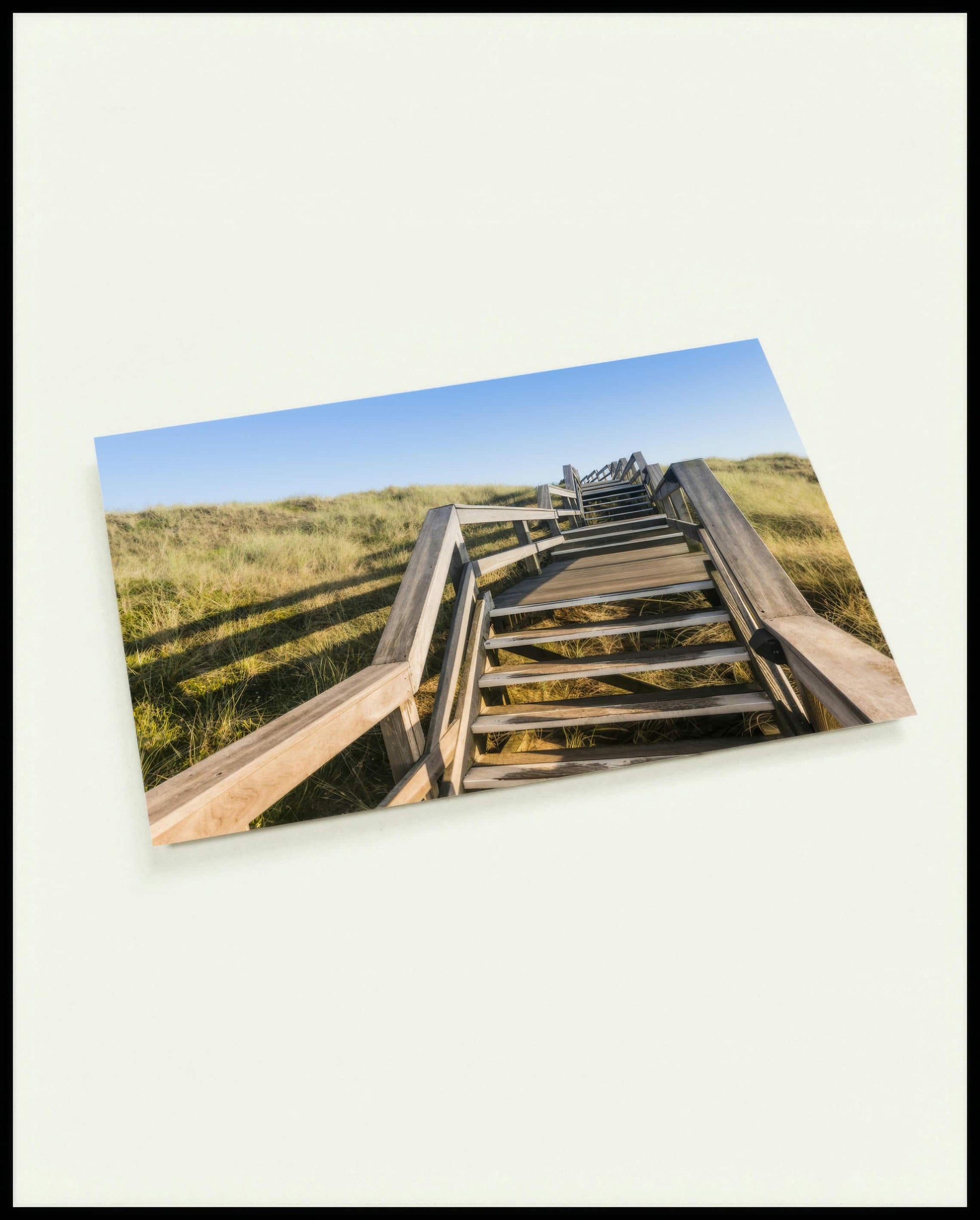 Eine Postkarte von einer Holztreppe die über Dünen am Strand führt.