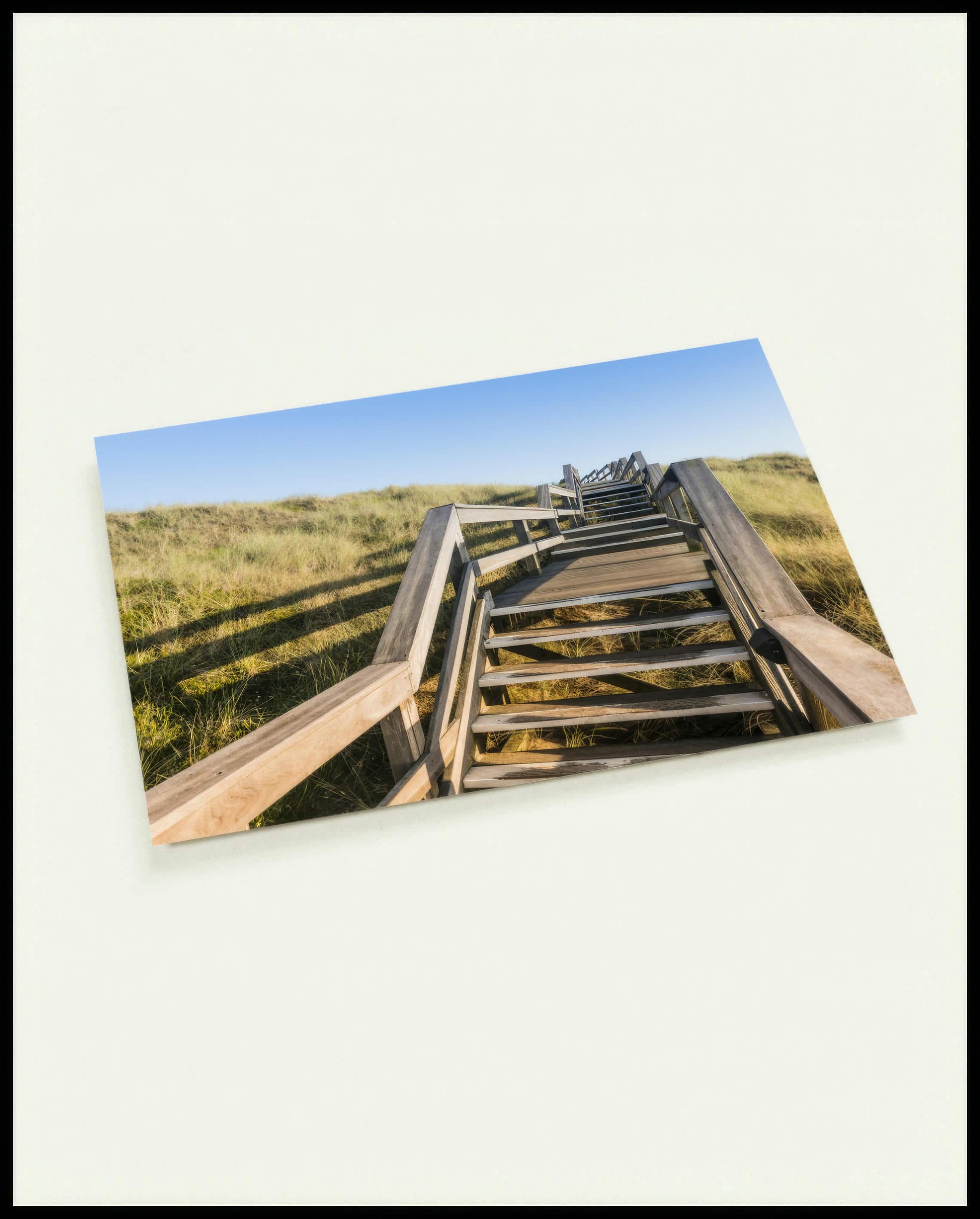 Eine Postkarte von einer Holztreppe die über Dünen am Strand führt.