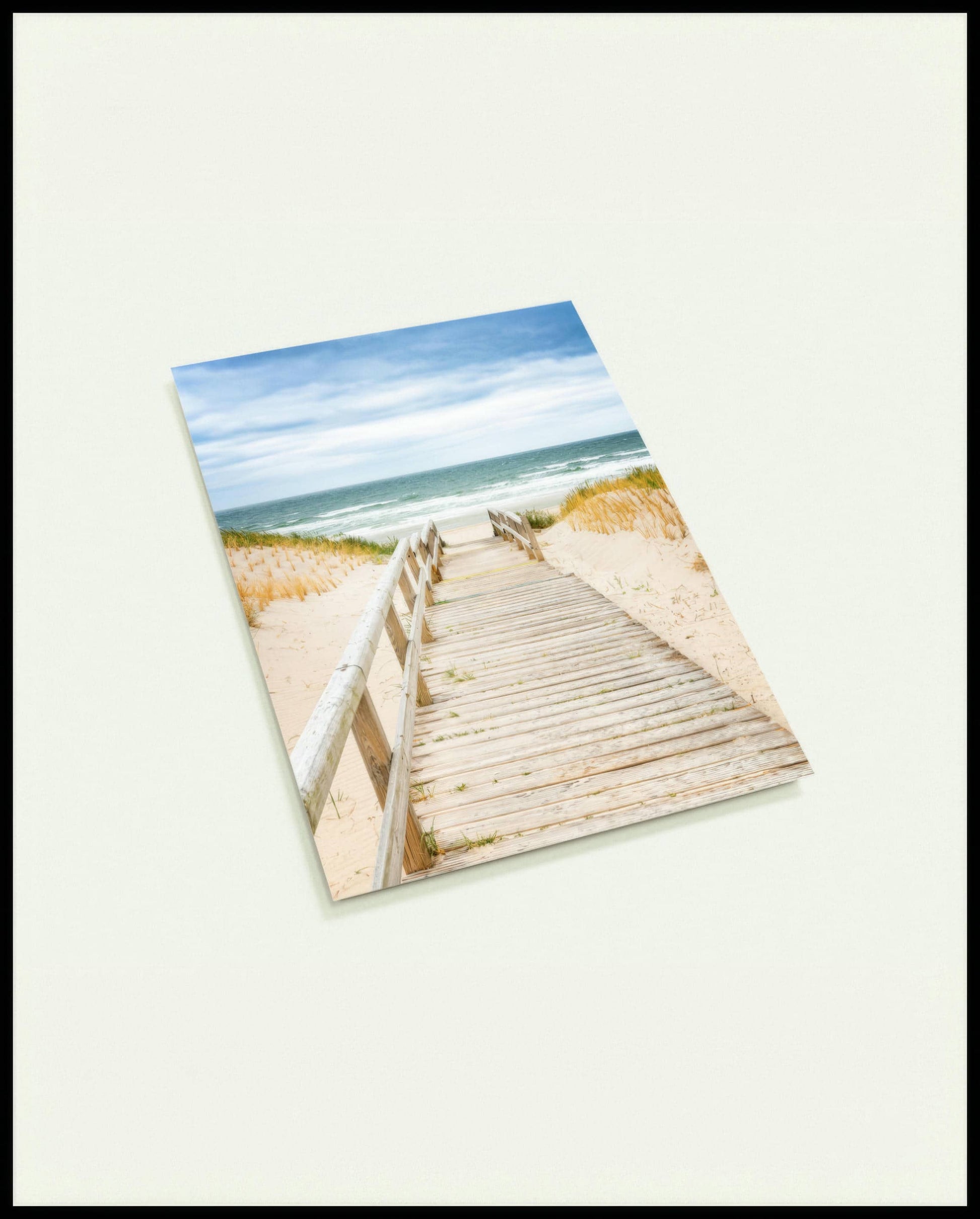 Eine Postkarte von einem Steg aus Holz der durch sandige Dünen zum Strand führt.