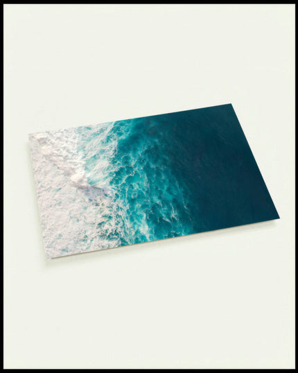 Eine Postkarte aus der Vogelperspektive vom blauen Meer und schaumigen Wellen.