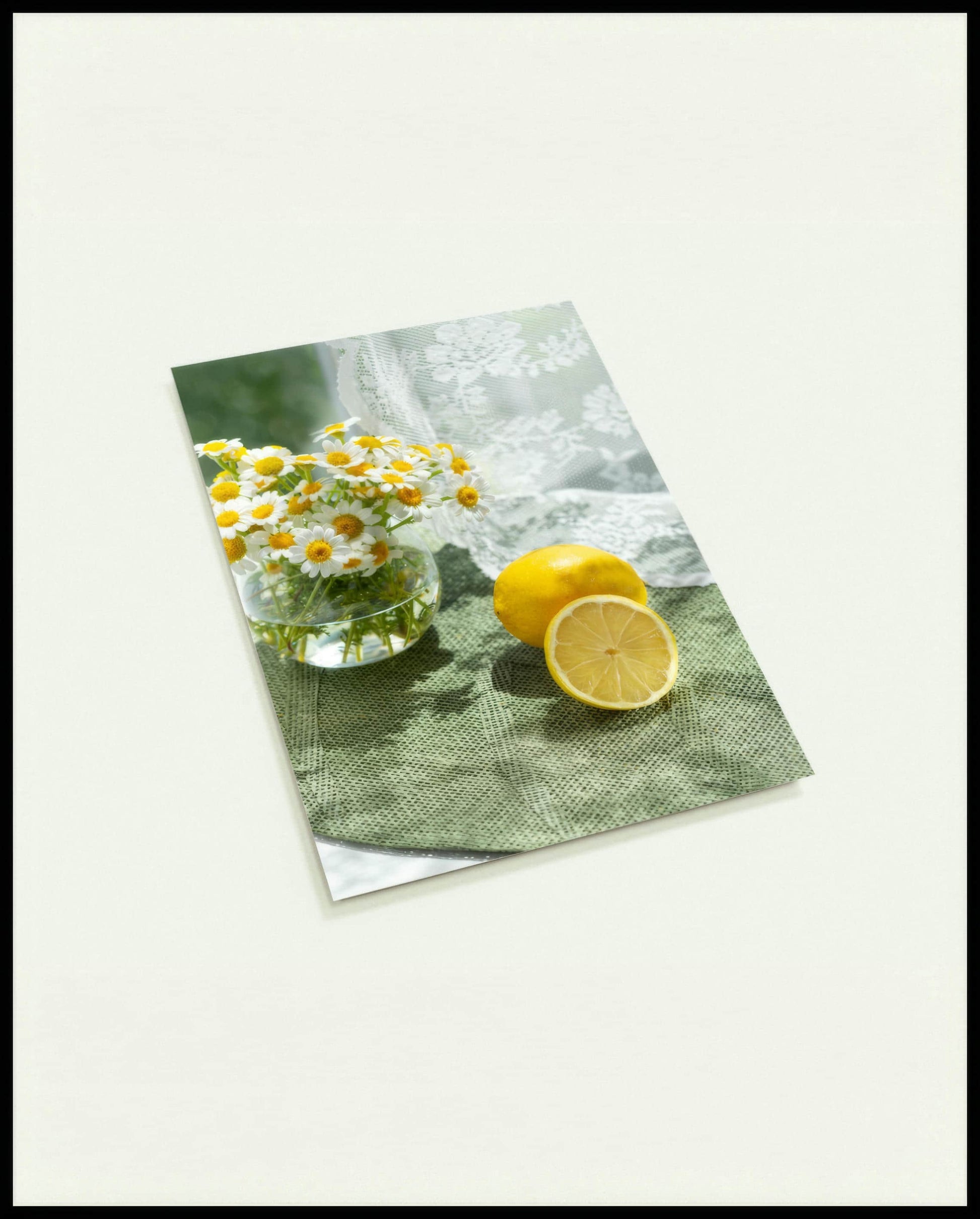Eine Postkarte von zwei Zitronen und Blumen in einem Glas auf einer grünen Unterlage aus Stoff.